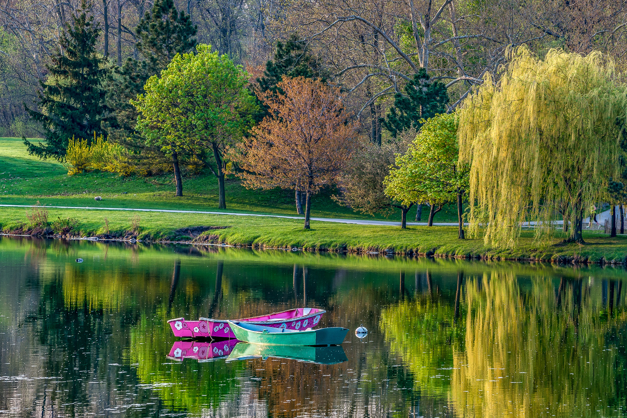 Two colorful boats on a calm lake, surrounded by green trees and yellow foliage.